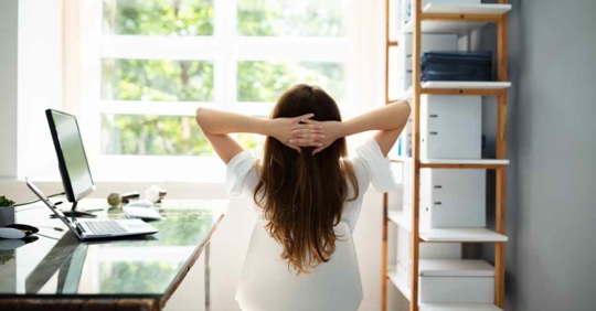 A woman relaxing in her home office. She is looking out the window to the yard